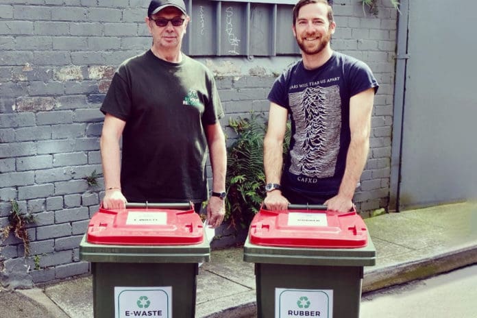 Two men standing with ewaste and rubber recycle bins