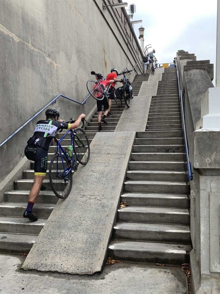 Cyclists pushing bikes up a steep staircase