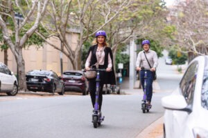 Two people wearing helmets riding on e-scooters