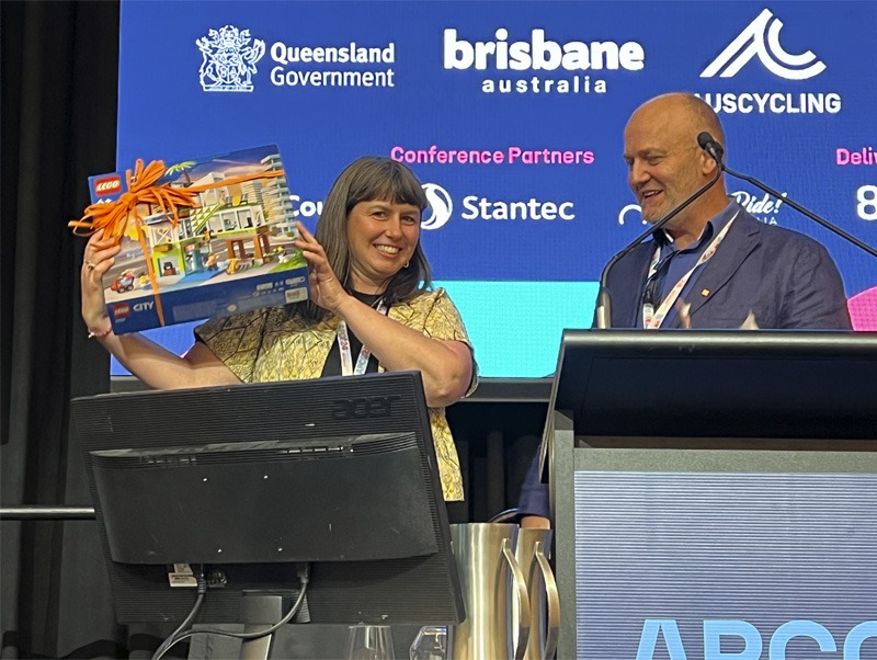 Two people on stage, one holding up a boxed Lego set