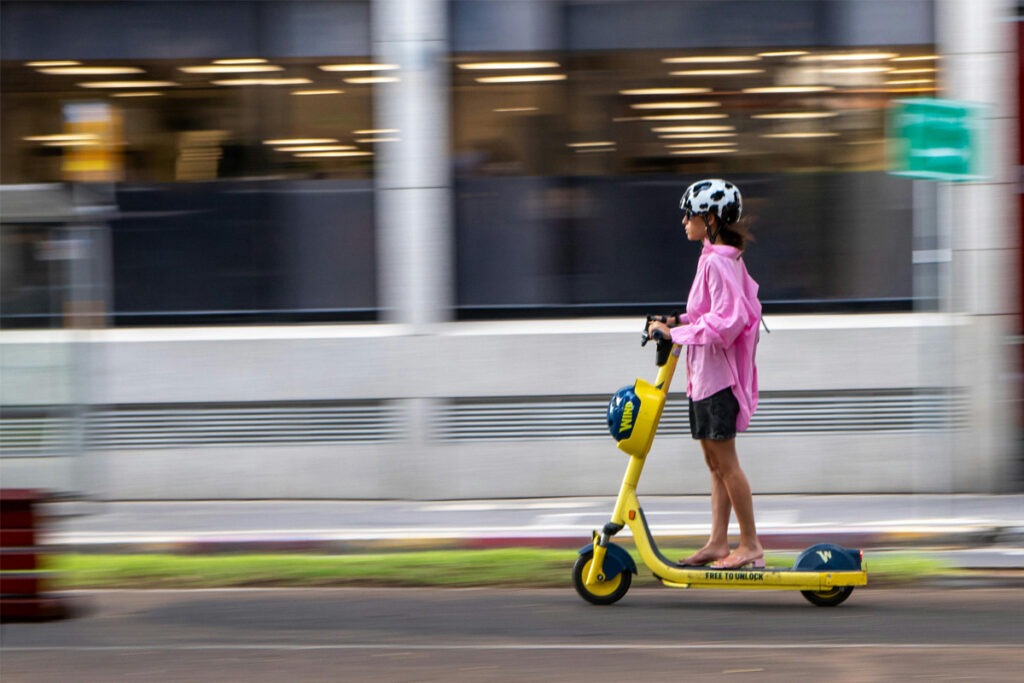 A person with helmet on riding e-scooter on street