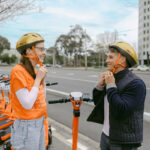 Two people putting on gold coloured helmets at e-scooter bay.