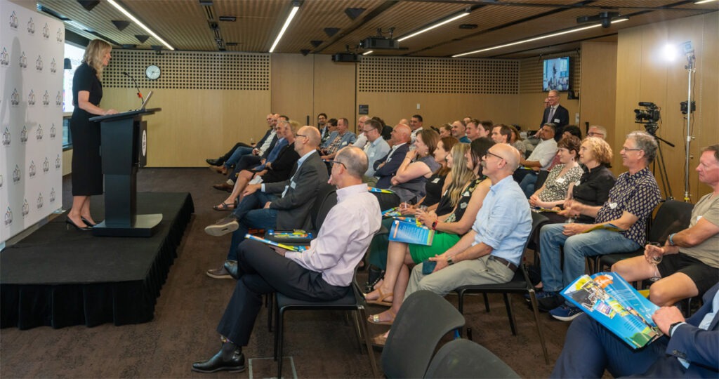 Group of people infront of person on stage speaking.